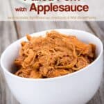 Slow cooker pulled pork with applesauce in white bowl on wooden table.