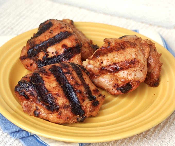 Three spicy grilled chicken thighs on a yellow plate.
