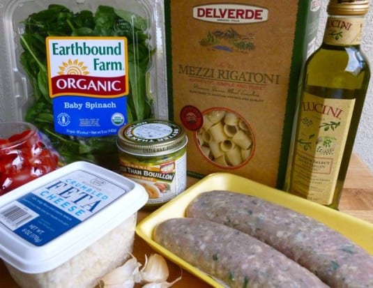Dinner making ingredients including chicken sausage, rigatoni pasta, spinach, cherry tomatoes, feta cheese and olive oil