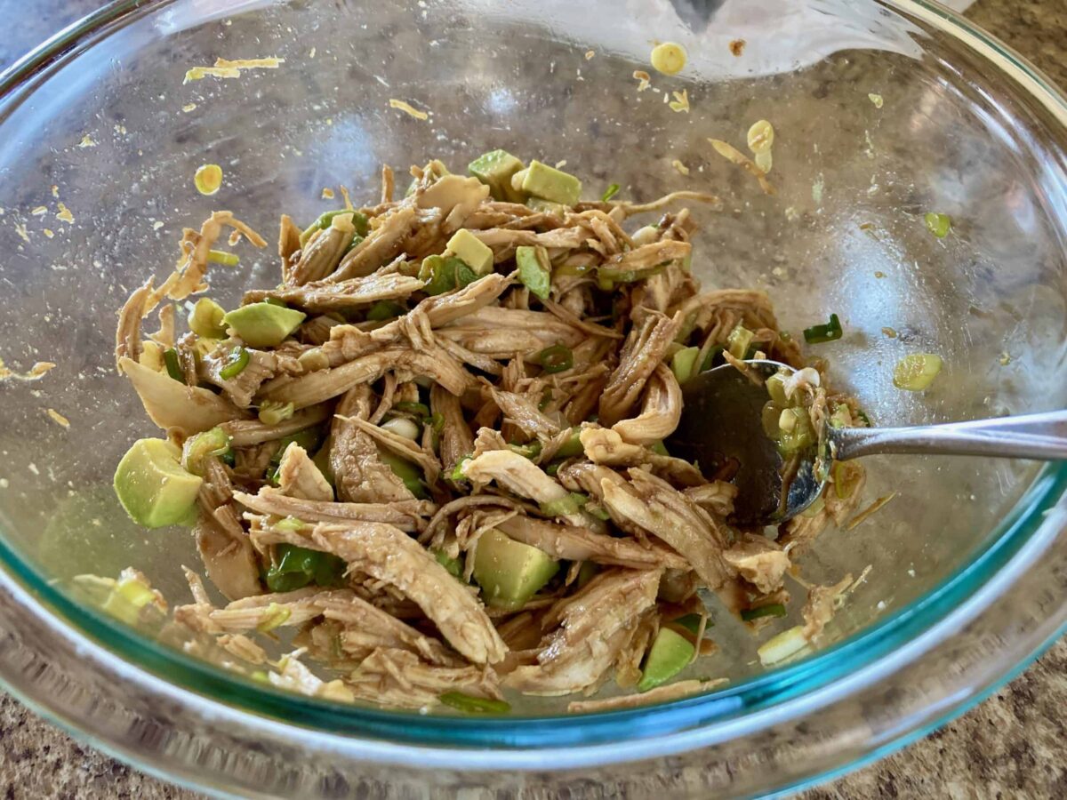 Shredded Chicken, Avocado, and Dressing in a large clear glass bowl.