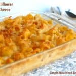 pyrex casserole dish filled with baked cauliflower macaroni and cheese on patterned tablecloth