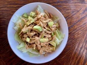 shredded chicken and avocado with Asian flavored dressing on a white plate shot from above