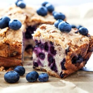 Piece of homemade blueberry crumb cake with fresh blueberries scattered around