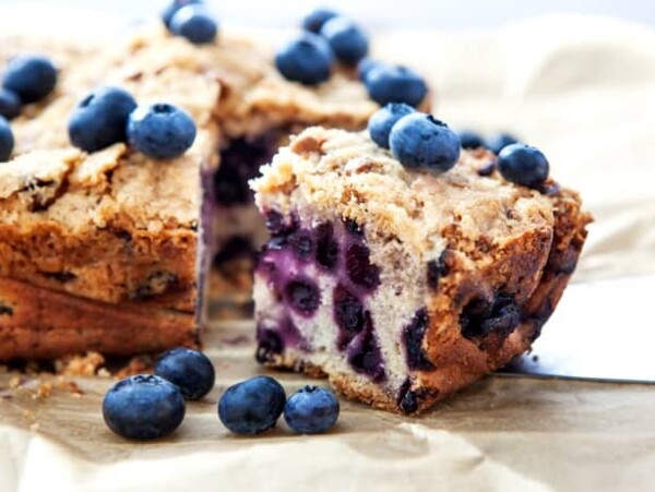 Piece of homemade blueberry crumb cake with fresh blueberries scattered around