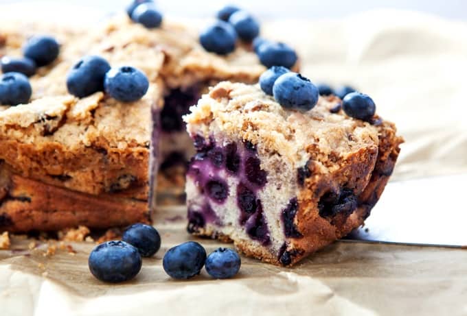 Piece of homemade blueberry crumb cake with fresh blueberries scattered around.