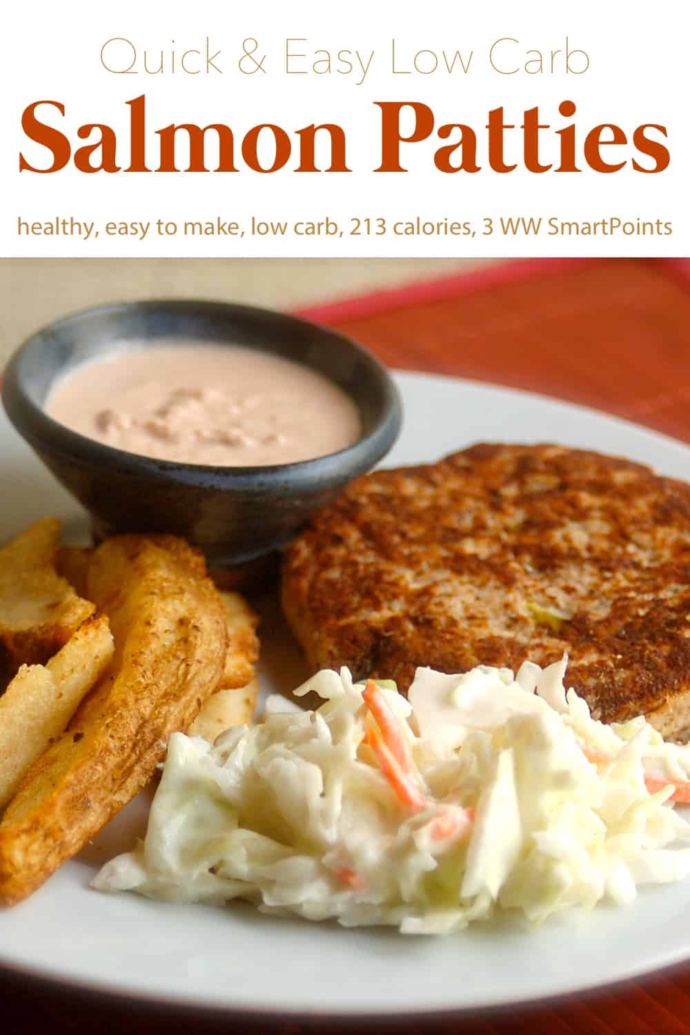 Salmon patty with cole slaw, potato wedges and horseradish sauce on white dinner plate.