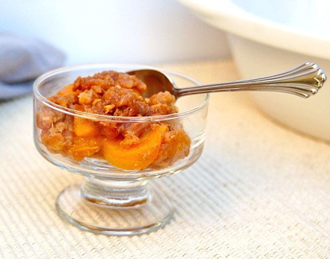 Crock Pot Peach Crisp in glass dessert dish with spoon.