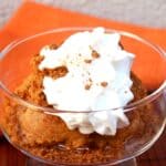 Pumpkin pie pudding with whipped topping in dessert glass with spoon and orange napkin.