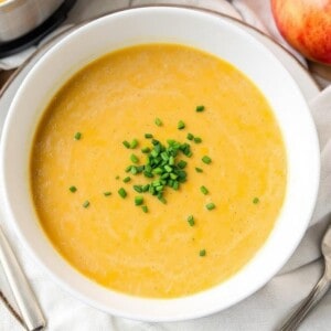 white bowl filled with squash apple soup garnished with chopped chives