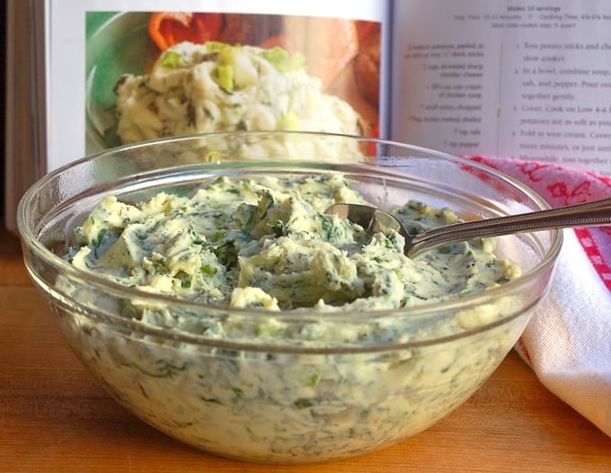 Mashed Potatoes made with spinach and dill in a glass bowl with a spoon, napkin on the side and cookbook in the background