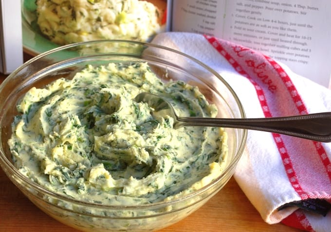 Glass bowl with spinach and dill mashed potatoes with a napkin and cookbook in the background