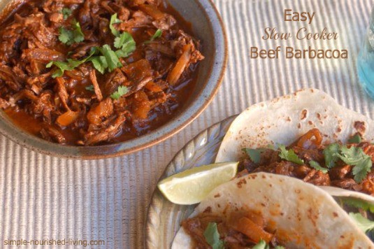 Easy Slow Cooker Beef Barbacoa with Frontera Beef Barbacoa Slow Cooking Sauce in serving bowl near plate of two beef barbacoa tacos.