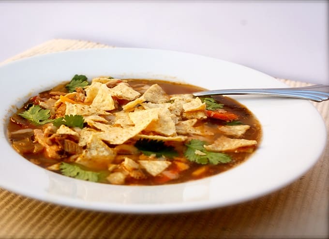 Chicken Tortilla Black Bean Soup garnished with fresh cilantro and crushed tortilla chips in white bowl with spoon.