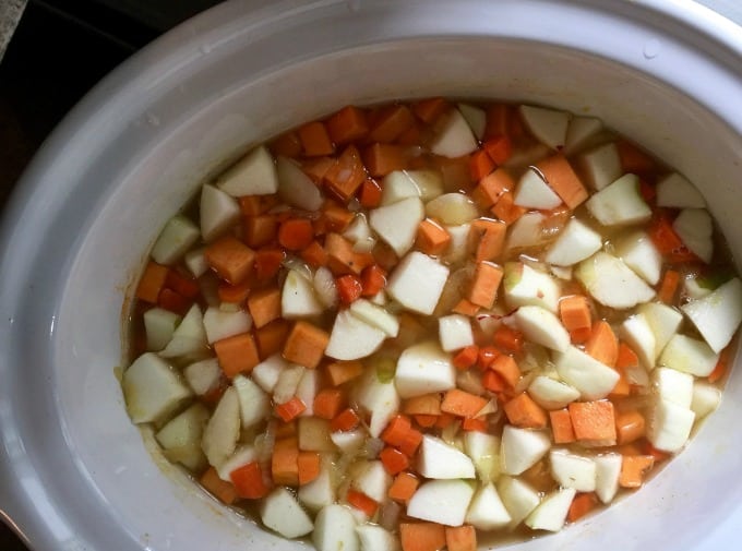Adding chopped onion, carrot, apple, sweet potato, broth in slow cooker for making curried carrot apple soup