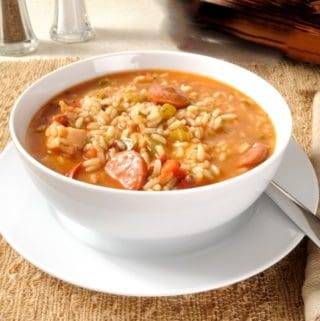 chicken sausage gumbo in white bowl on saucer with spoon
