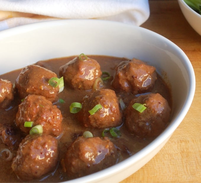 Slow cooker cranberry meatballs in creamy gravy in white serving dish.