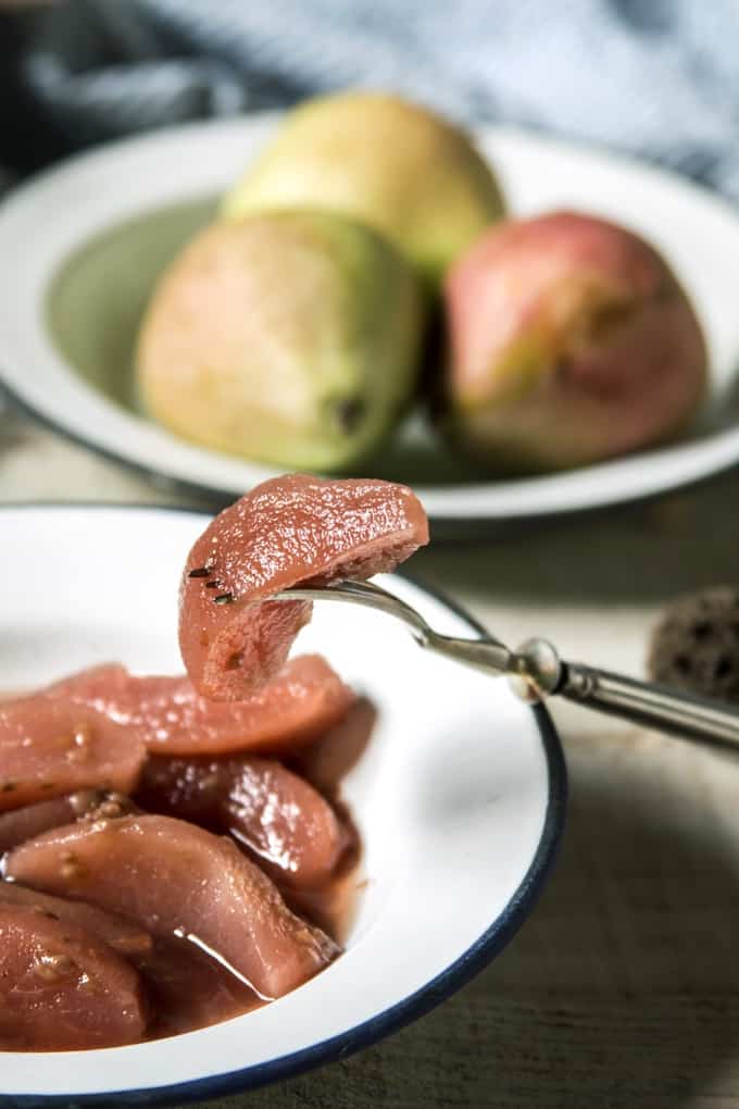 Hand with a fork, eating poached pears with whole pears in the background