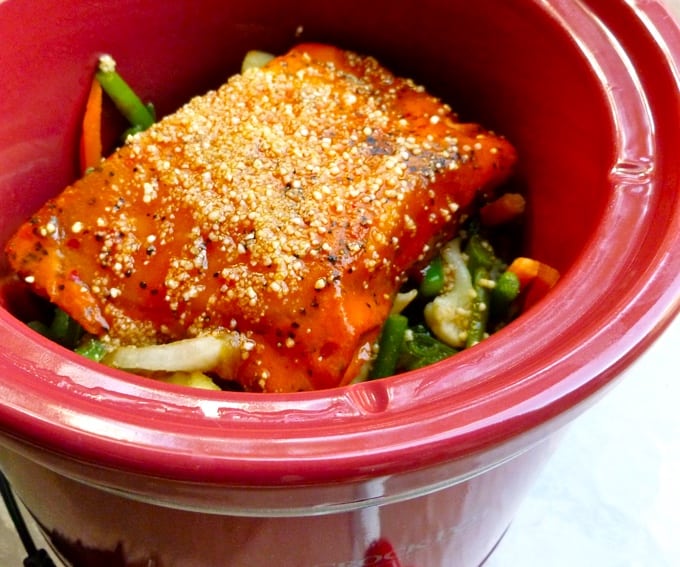 Red crock pot with salmon fillet with sesame seeds over Asian style vegetables.