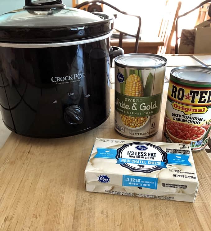 Ingredients for making crock pot corn dip, including crock pot, canned corn, Rotes canned tomatoes with green chilies and Neufchatel cream cheese.