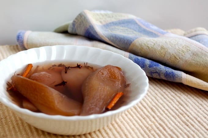 Poached pears with cinnamon and clove in a while bowl with a dish towel in the background