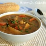 Hearty Slow Cooker Beef Stew in white bowl with baguette in background