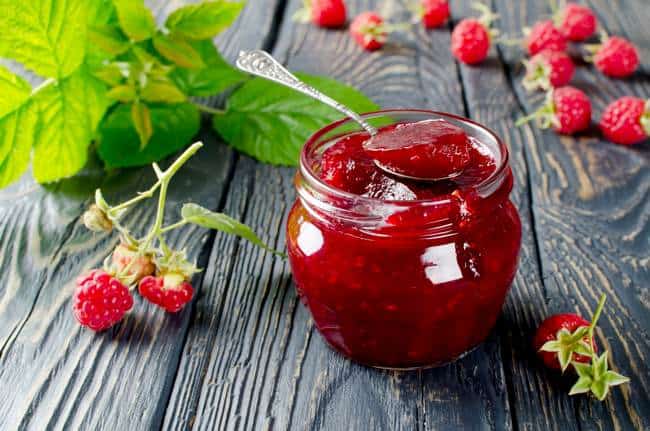 Homemade Raspberry Jam in a jar on a wooden table surrounded by fresh raspberries