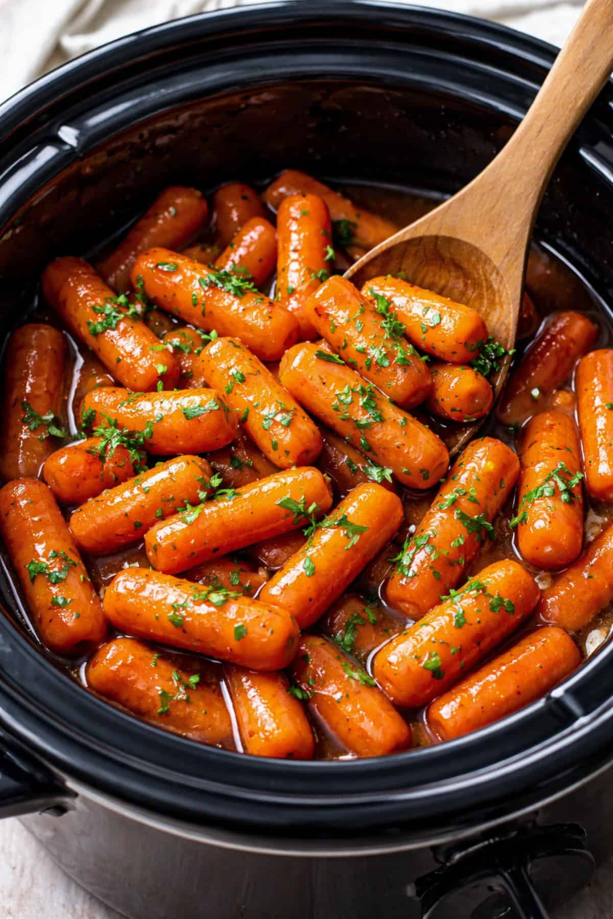 Slow Cooker Apple Glazed Carrots in a black crock pot with wooden serving spoon.