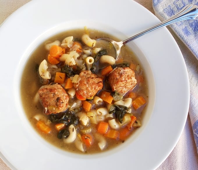 Slow Cooker Italian Wedding Soup with turkey meatballs in white bowl with spoon from above.