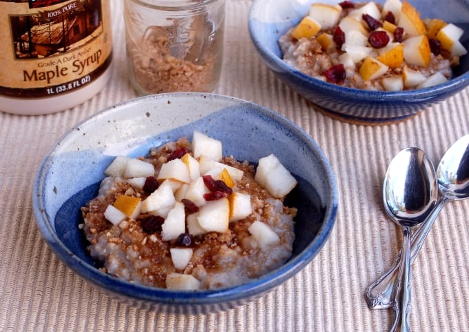 Two bowls with slow cooker multigrain cereal topped with dried cranberries and fresh fruit in blue bowls with spoons.
