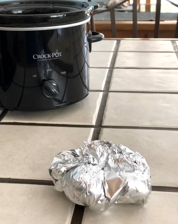 Garlic Wrapped Tightly in Foil Packet with Crock Pot in the background
