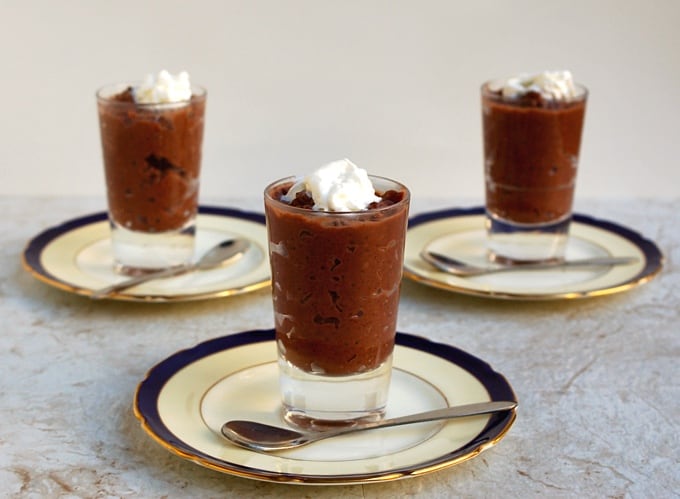 Three servings of chocolate rice pudding in dessert glasses on small plates with spoons.