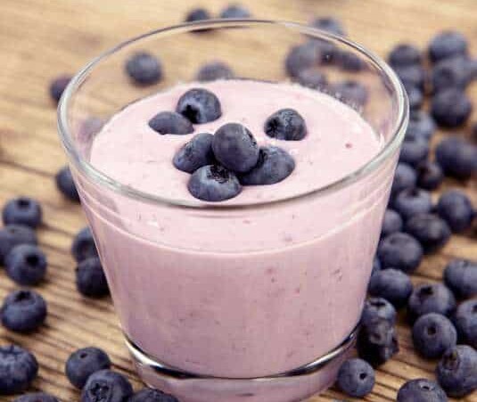 Blueberry BanaGlass of Almond Butter Smoothie topped and surrounded by fresh blueberries