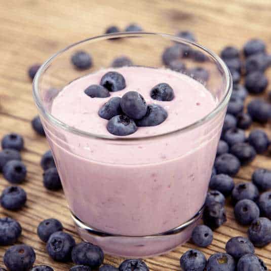 Glass of Blueberry Banana Almond Butter Smoothie topped and surrounded by fresh blueberries.