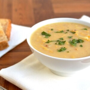 corn chowder in white bowl on white napkin with slices of toast in background