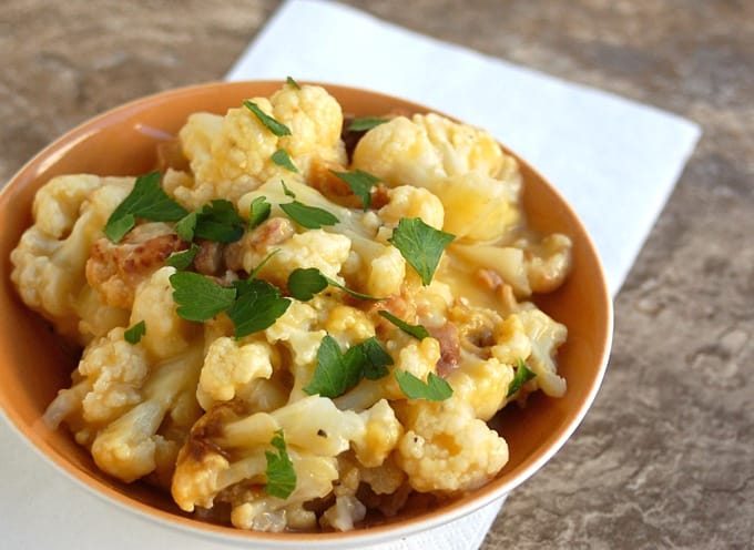 Bowl of cheesy cauliflower with bacon, topped with parsley