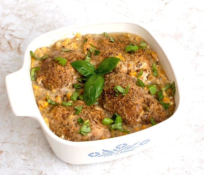 Crock Pot Chicken Thighs with Creamy Corn in casserole dish topped with fresh basil