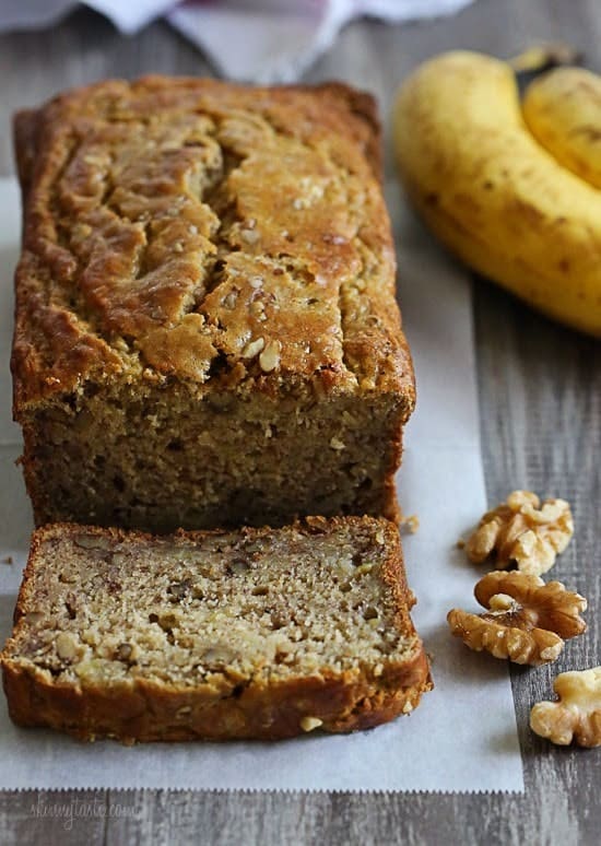 loaf of gluten free banana bread on parchment with slice in foreground and walnut halves and bananas alongside