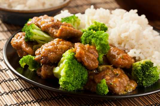 Beef and Broccoli with white rice on black plate on bamboo placemat.