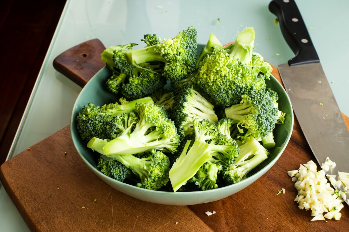 bowl of broccoli on cutting board with minced garlic and chef's knife alongside