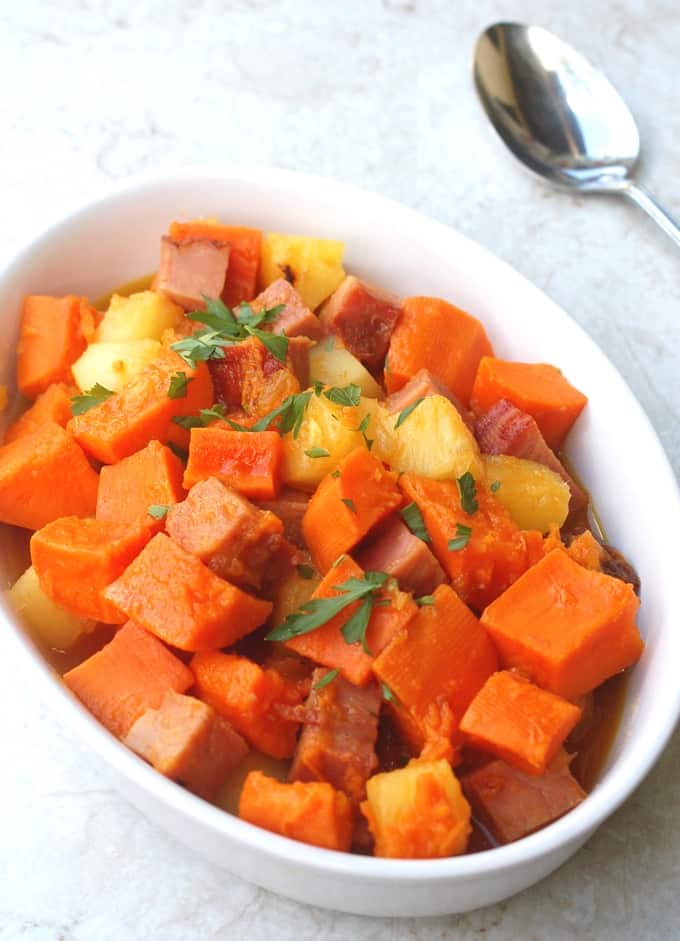 Sweet potatoes, ham and pineapple in a white serving dish with spoon