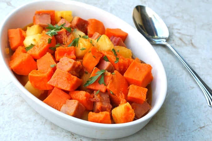 Ham and sweet potatoes with pineapple in a white serving dish with a spoon