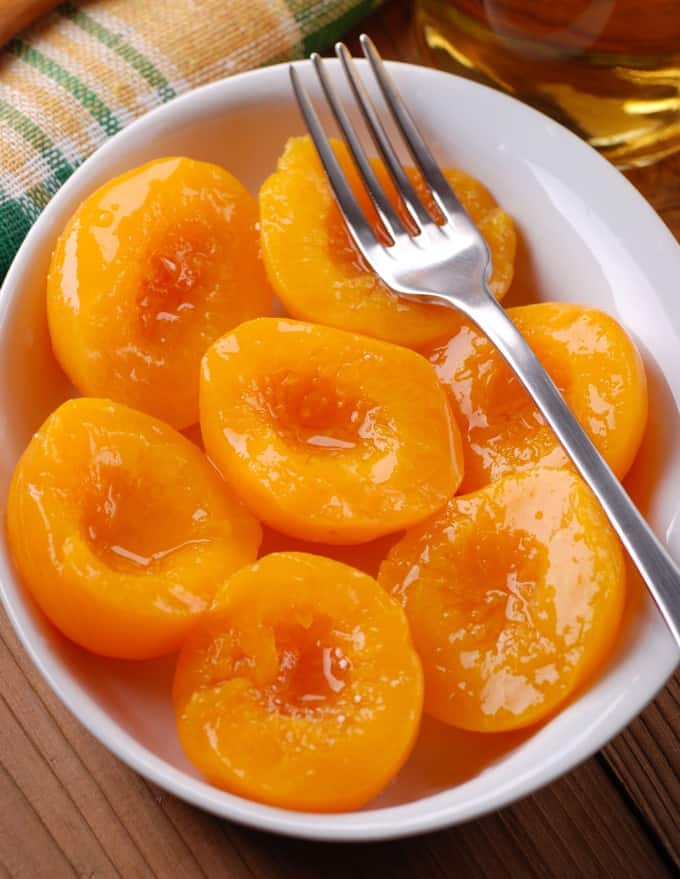 Slow cooker peaches in white serving dish with fork.