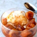 Slow cooker bananas foster over vanilla ice cream in small glass dish with spoon.