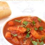 Bowl with saucy chicken cacciatore stew garnished with fresh parsley and piece of bread in background