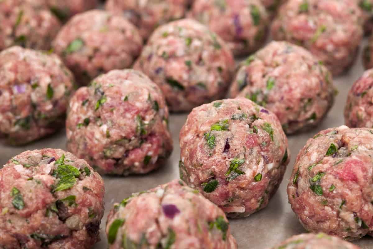 Uncooked lean ground beef meatballs on parchment paper.
