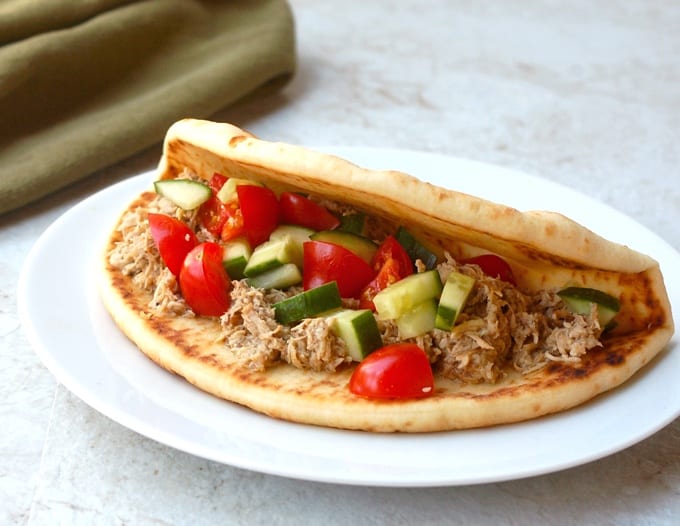 Greek chicken pita sandwich with chopped cucumber and tomatoes on white plate.