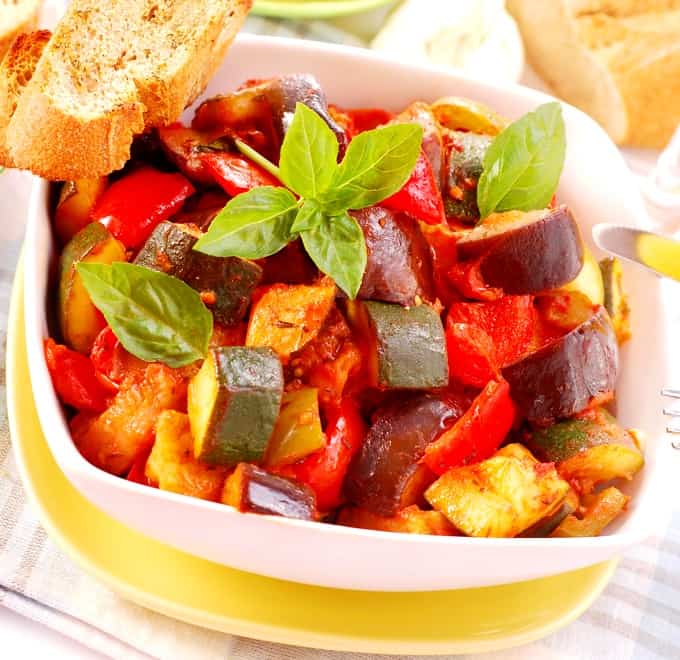 Dish of ratatouille garnished with fresh basil leaves and crusty bread