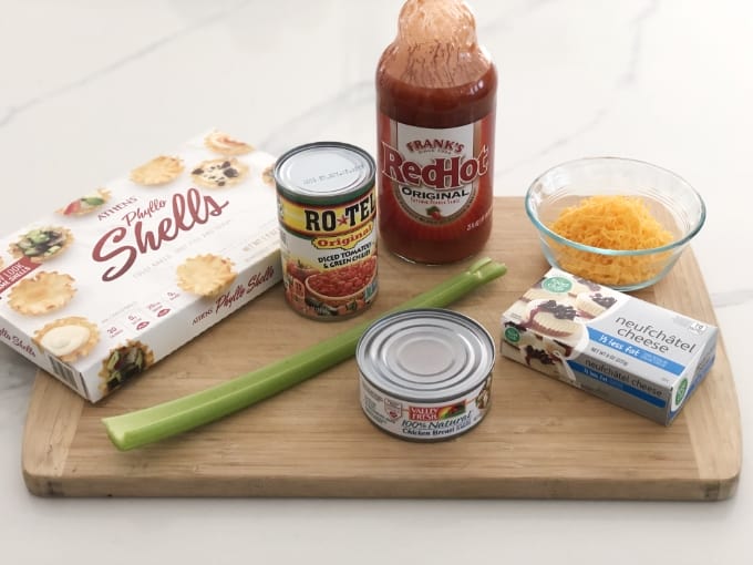 Mini Phyllo Shellos, can of Rotes, Frank's red hot pepper sauce, celery stalk, can of chicken breast, neufchâtel cheese and shredded cheddar on cutting board.