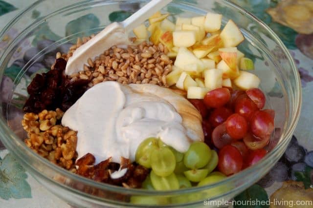 Red and green grapes, chopped apples, grains, walnuts and yogurt arranged in a clear bowl before mixing