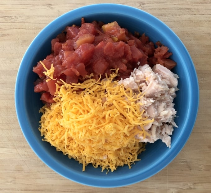 Rotel tomatoes, shredded cheese, canned chuck chicken in blue bowl.